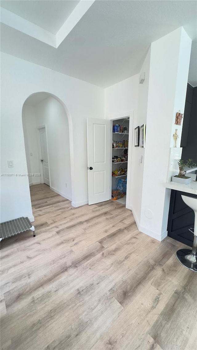 spare room with arched walkways, light wood-type flooring, and baseboards