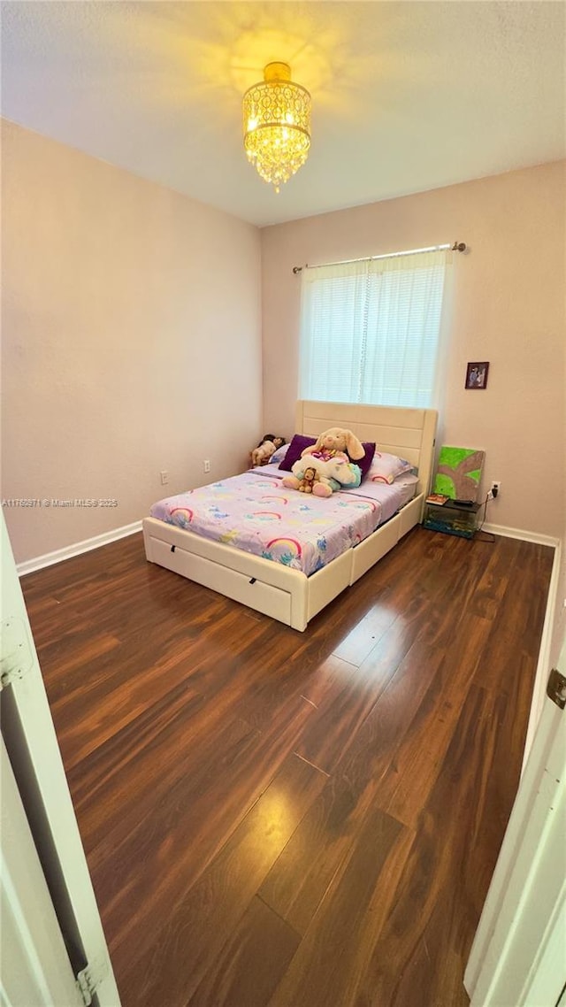 unfurnished bedroom featuring an inviting chandelier, wood finished floors, and baseboards