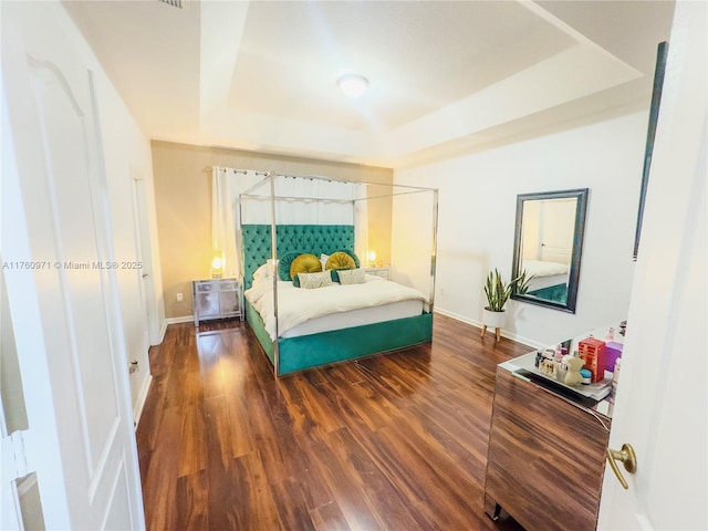 bedroom with baseboards, a tray ceiling, and wood finished floors