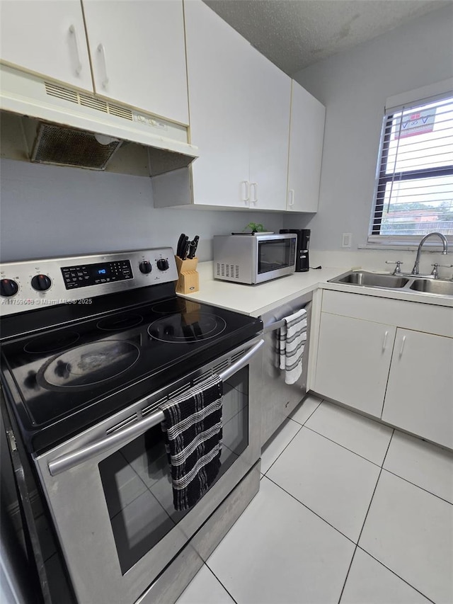 kitchen featuring under cabinet range hood, light tile patterned floors, appliances with stainless steel finishes, white cabinets, and a sink