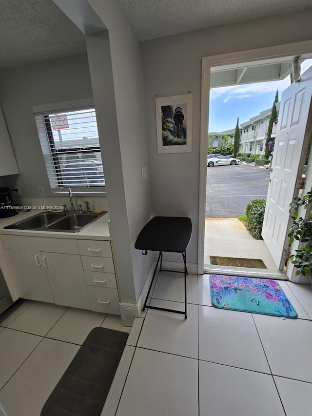 doorway with a sink, baseboards, a textured ceiling, and light tile patterned floors