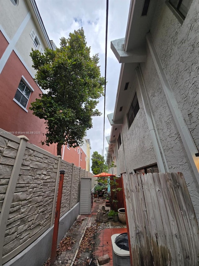 view of side of home with a fenced backyard, central AC, and stucco siding