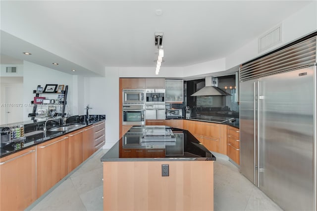 kitchen featuring visible vents, wall chimney range hood, built in appliances, modern cabinets, and a sink