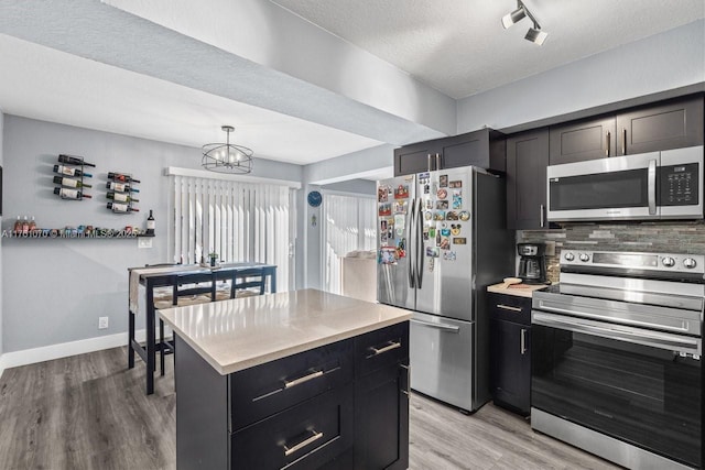 kitchen featuring light wood finished floors, stainless steel appliances, light countertops, dark cabinets, and a chandelier