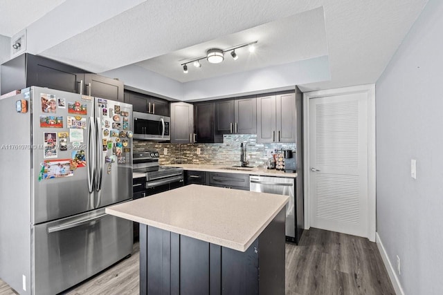 kitchen with a sink, wood finished floors, appliances with stainless steel finishes, light countertops, and decorative backsplash