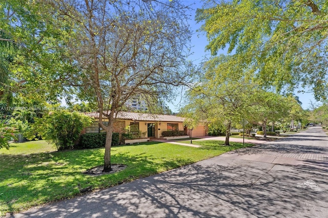 view of front of house featuring a tile roof, a front yard, driveway, and stucco siding