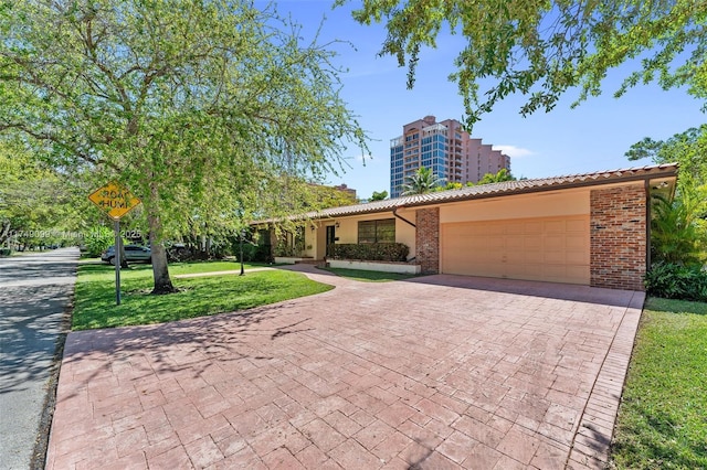 view of front of home featuring a front yard, an attached garage, a tiled roof, decorative driveway, and brick siding