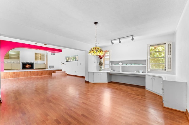 unfurnished living room with track lighting, light wood-style flooring, and a warm lit fireplace