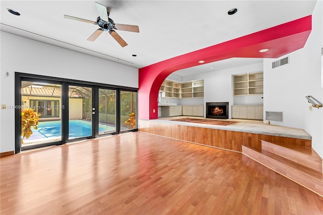 unfurnished living room with built in features, wood finished floors, visible vents, and a lit fireplace