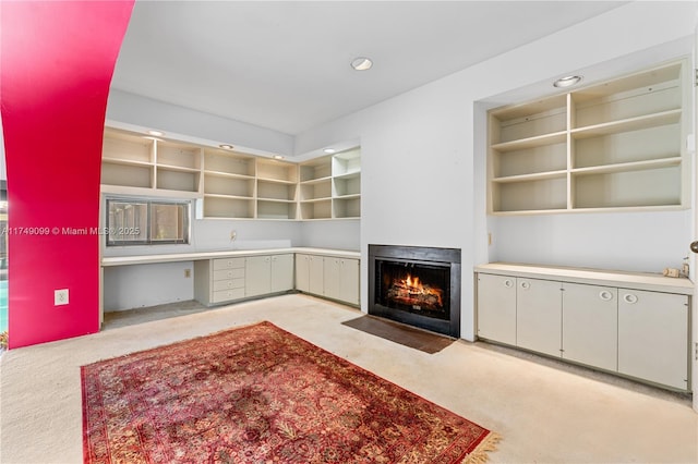 unfurnished living room with recessed lighting, a fireplace with flush hearth, light colored carpet, and built in desk