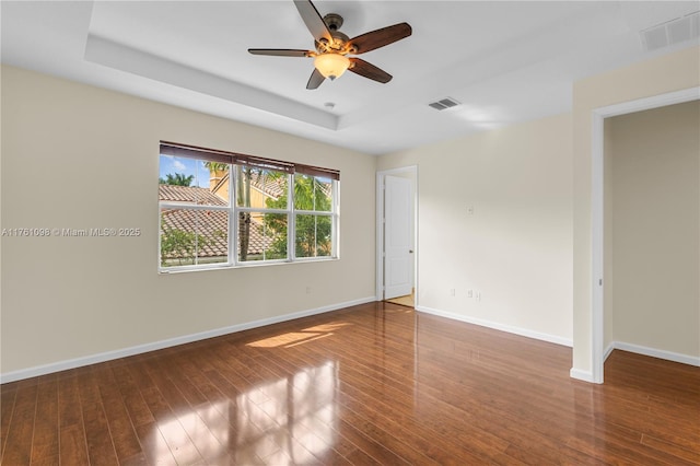 unfurnished room with baseboards, a tray ceiling, wood-type flooring, and visible vents