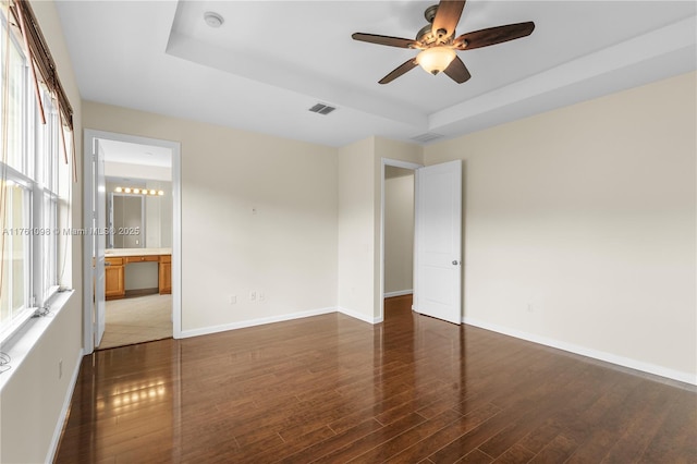 spare room featuring a tray ceiling, baseboards, visible vents, and wood finished floors