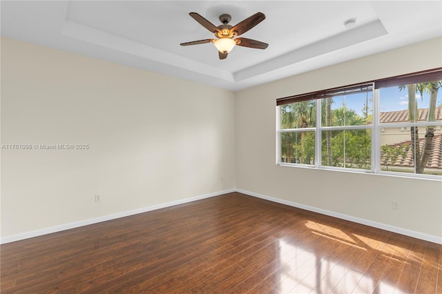 empty room featuring baseboards, a raised ceiling, ceiling fan, and dark wood-style flooring