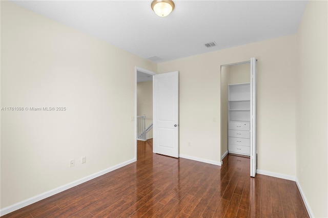 unfurnished bedroom with wood finished floors, visible vents, a closet, and baseboards