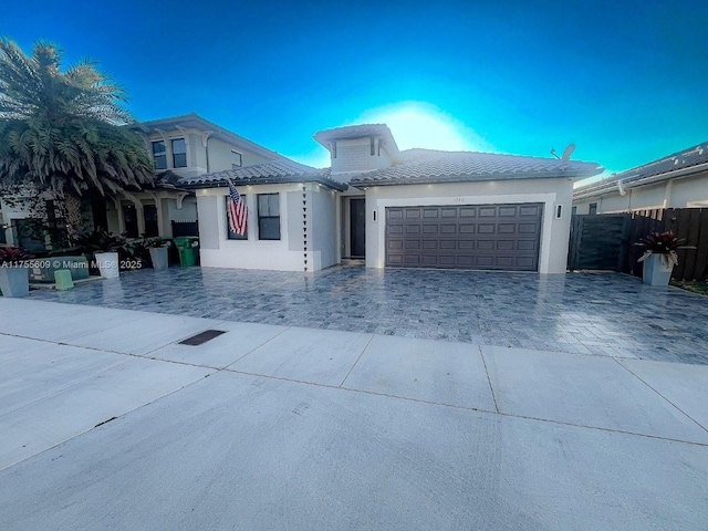 view of front facade featuring fence, an attached garage, stucco siding, a tile roof, and decorative driveway