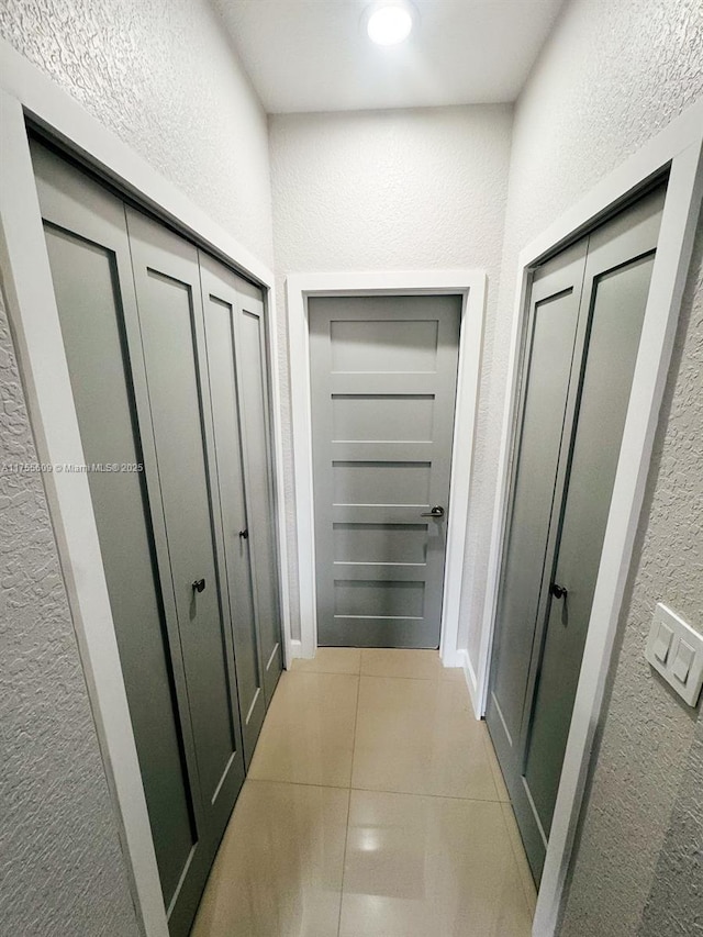 hall featuring baseboards, light tile patterned flooring, and a textured wall