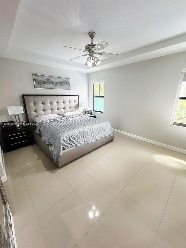 tiled bedroom featuring a tray ceiling, baseboards, a textured ceiling, and a ceiling fan