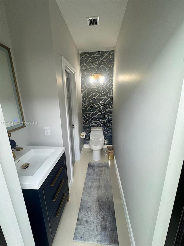 bathroom featuring visible vents, an accent wall, baseboards, toilet, and vanity