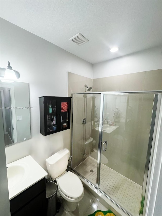 full bath featuring vanity, visible vents, a stall shower, a textured ceiling, and toilet