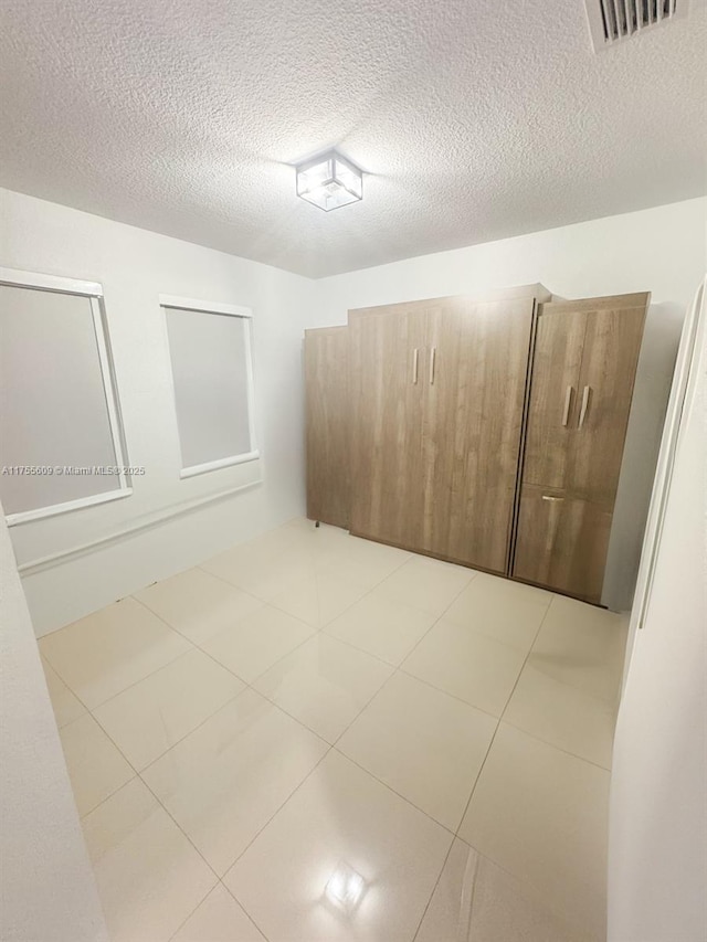 spare room with tile patterned floors, visible vents, and a textured ceiling