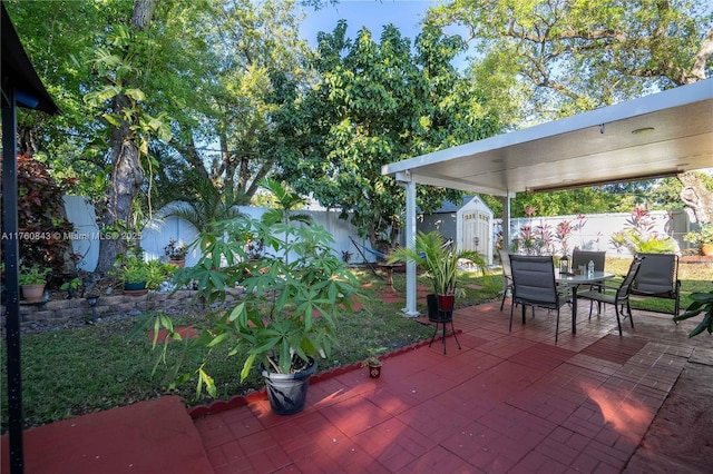 view of patio with an outbuilding, a storage unit, outdoor dining area, and a fenced backyard