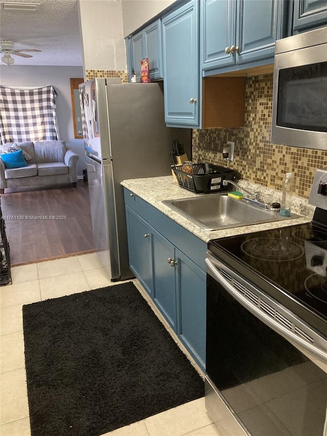 kitchen featuring blue cabinets, stainless steel appliances, open floor plan, and decorative backsplash