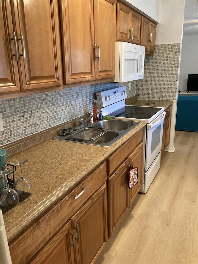 kitchen featuring white appliances, brown cabinetry, a sink, decorative backsplash, and light wood-type flooring