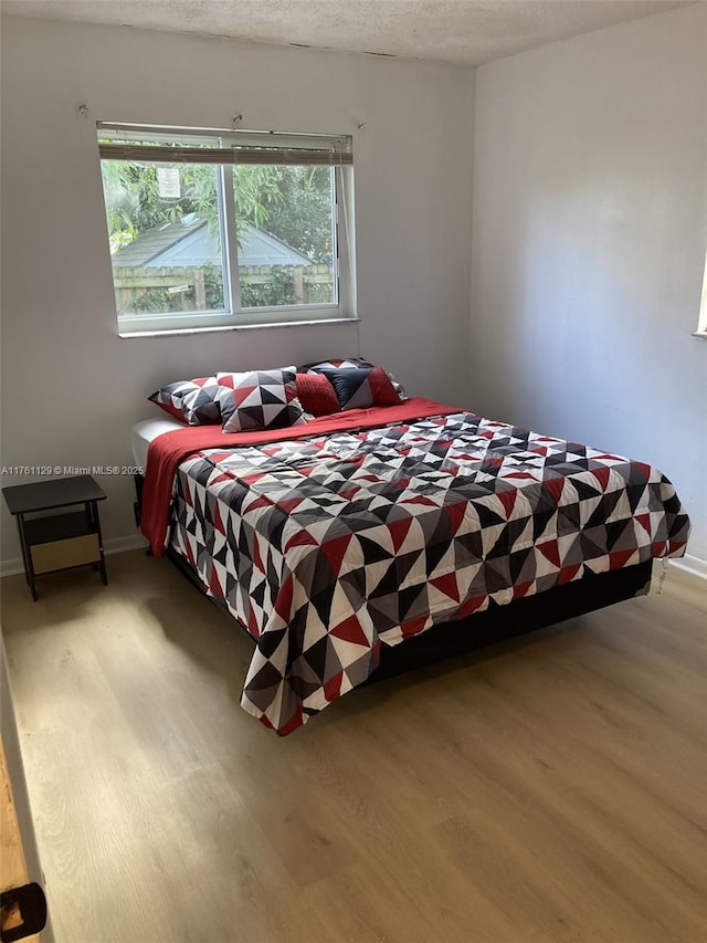 bedroom with light wood-type flooring, baseboards, and a textured ceiling