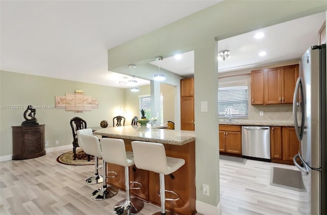 kitchen with a sink, light wood finished floors, appliances with stainless steel finishes, and a kitchen bar