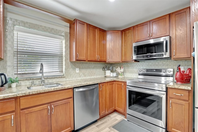 kitchen featuring decorative backsplash, a sink, light stone counters, stainless steel appliances, and light wood-style flooring