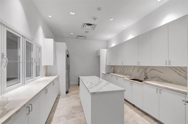 kitchen featuring a sink, marble finish floor, recessed lighting, backsplash, and a kitchen island