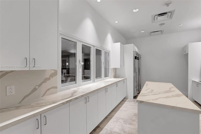 kitchen with visible vents, a center island, light stone counters, white cabinets, and recessed lighting