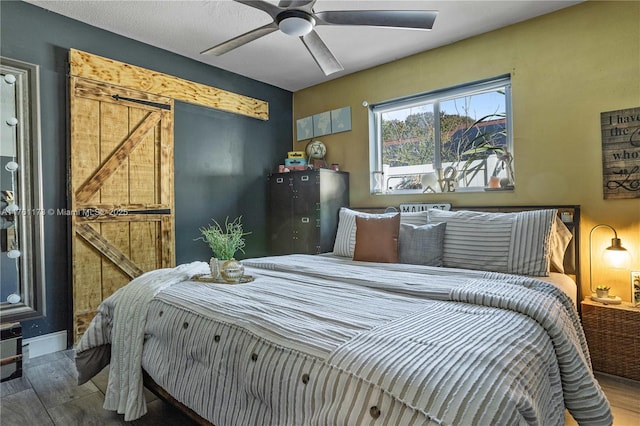 bedroom featuring a barn door, wood finished floors, and a ceiling fan