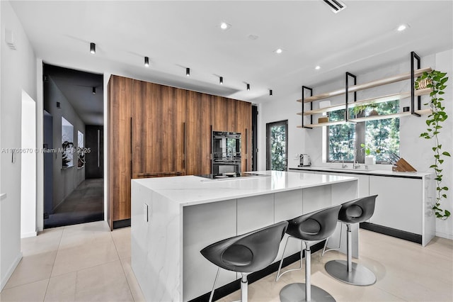 kitchen with a kitchen island, open shelves, light tile patterned flooring, dobule oven black, and modern cabinets