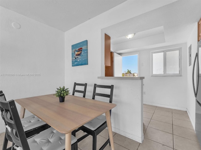 dining space with light tile patterned floors, a tray ceiling, and baseboards