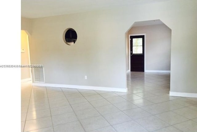 empty room featuring light tile patterned floors, baseboards, arched walkways, and visible vents