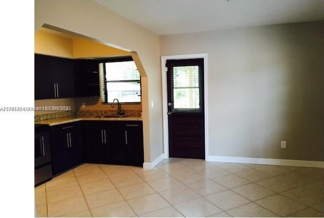 kitchen featuring dark cabinetry, light tile patterned floors, baseboards, and a sink