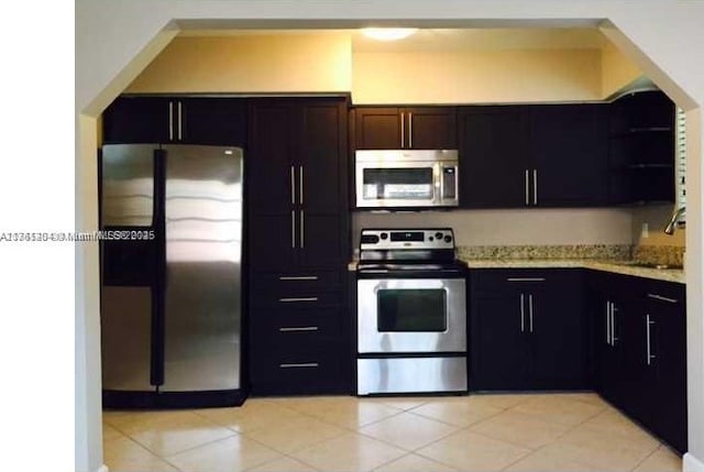 kitchen featuring a sink, light stone counters, appliances with stainless steel finishes, and light tile patterned floors