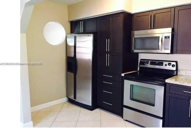 kitchen featuring light tile patterned floors, light stone countertops, baseboards, stainless steel appliances, and dark brown cabinets