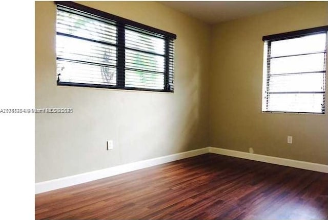 spare room with dark wood finished floors, a wealth of natural light, and baseboards