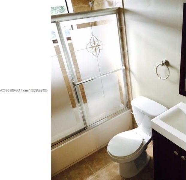 full bath with tile patterned floors, combined bath / shower with glass door, toilet, and vanity