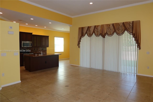 interior space with an island with sink, ornamental molding, stainless steel microwave, range, and tasteful backsplash