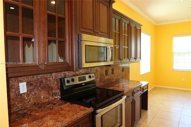 kitchen with baseboards, ornamental molding, stainless steel appliances, glass insert cabinets, and backsplash