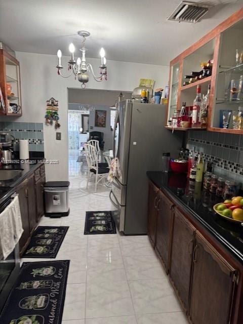 kitchen with visible vents, tasteful backsplash, dark countertops, glass insert cabinets, and a chandelier