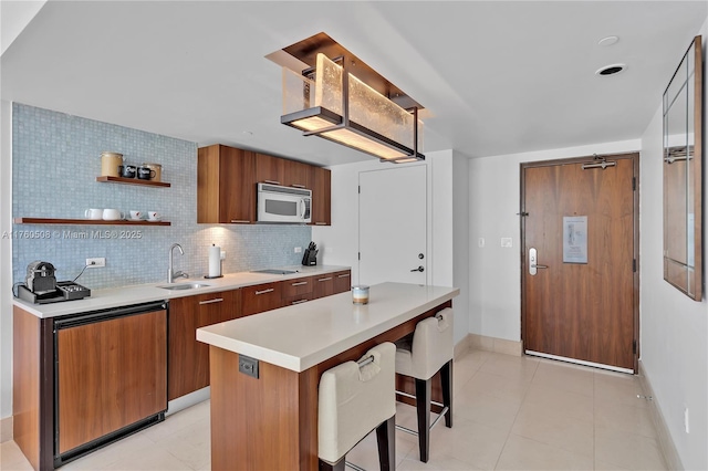 kitchen with modern cabinets, a sink, backsplash, light countertops, and white microwave