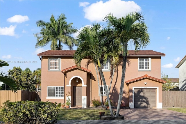 mediterranean / spanish-style home featuring stucco siding, an attached garage, and fence