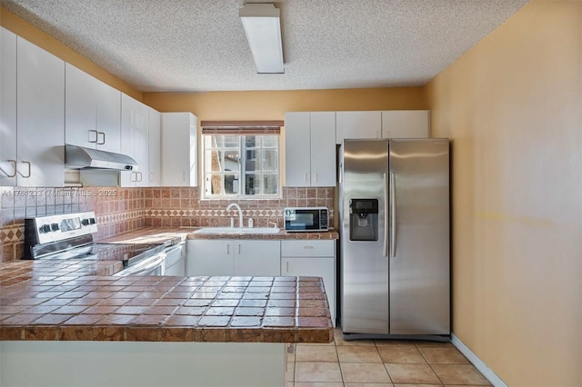 kitchen featuring a peninsula, a textured ceiling, under cabinet range hood, a sink, and appliances with stainless steel finishes