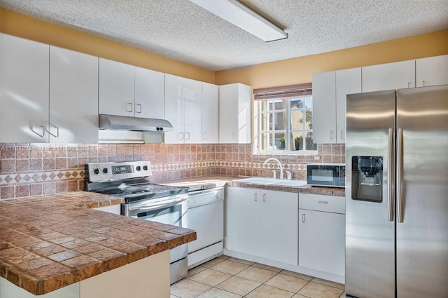 kitchen featuring under cabinet range hood, a sink, tasteful backsplash, stainless steel appliances, and a peninsula