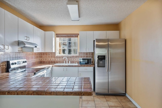 kitchen featuring under cabinet range hood, a sink, tasteful backsplash, appliances with stainless steel finishes, and a peninsula