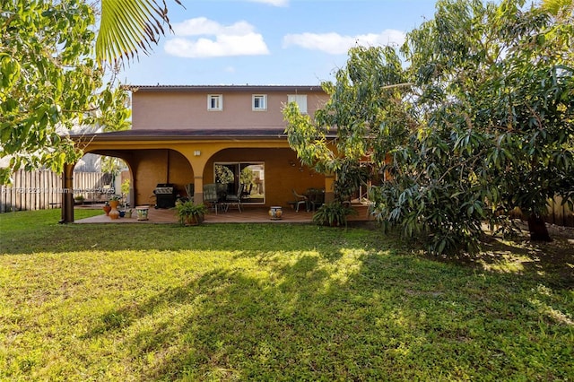 rear view of property with a yard, fence, and stucco siding